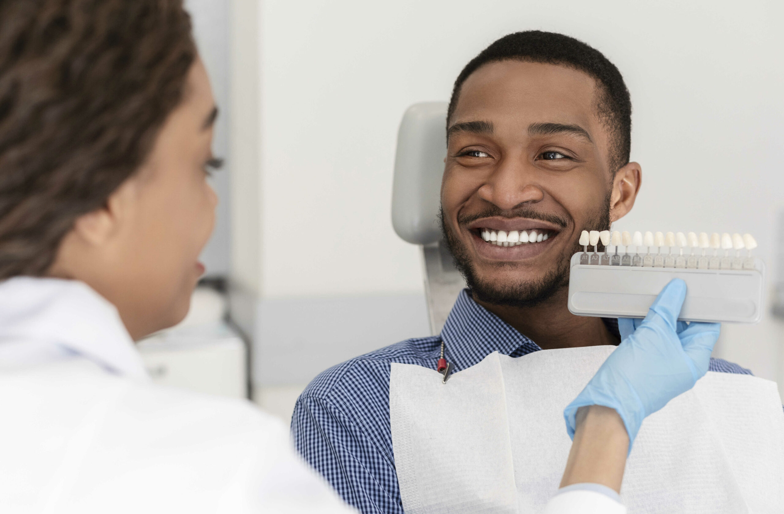 Cheerful african patient and dentist choosing filling shade in Chicago